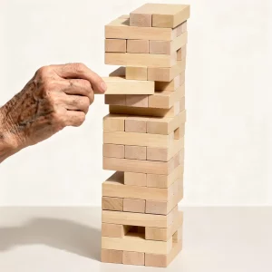 Tour chancelante en bois : jeu d'adresse et d'équilibre, avec une main âgée retirant une pièce du haut d’une tour de blocs.